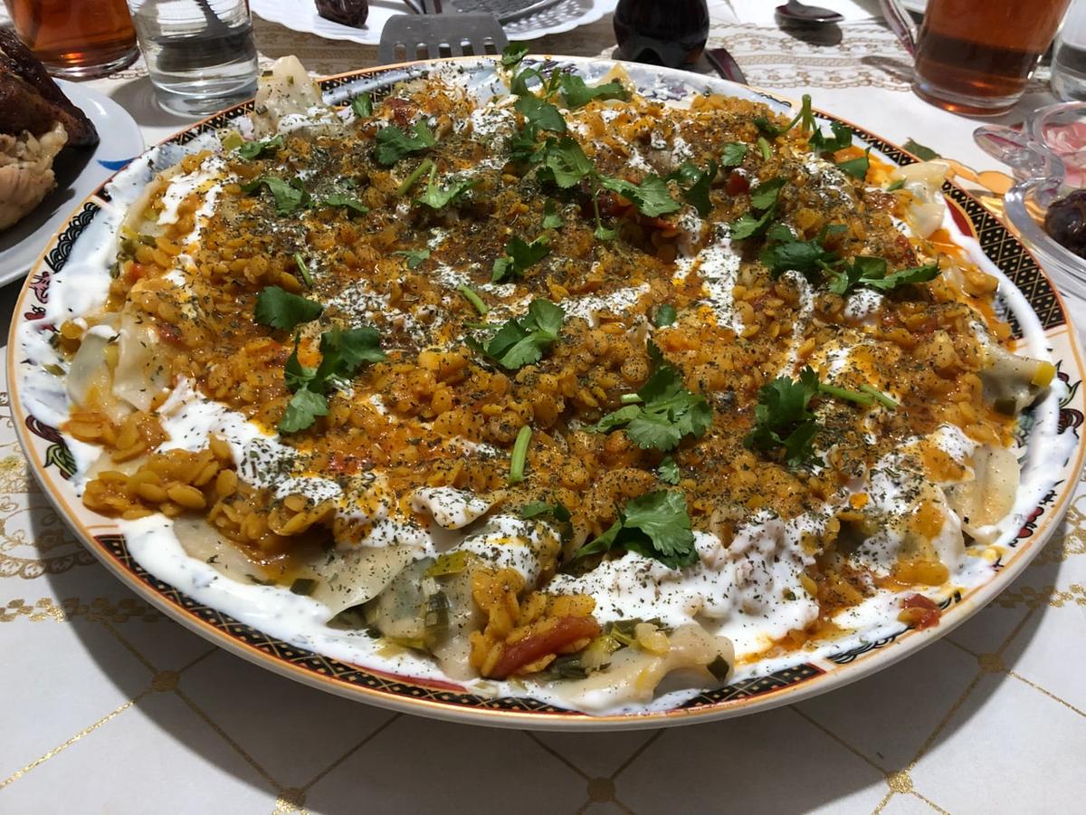 Große Platte mit Teigtaschen, bedeckt mit Joghurt, Soße, Kräutern und herzhaftem Garnitur.