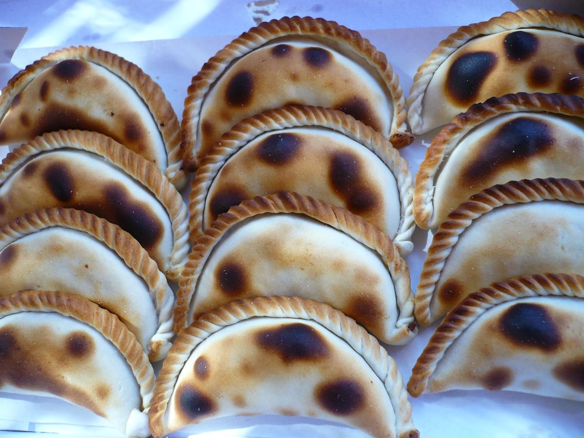 Reihen kleiner gebackener Halbmond-Teigtaschen mit Krempe auf einem Blech.
