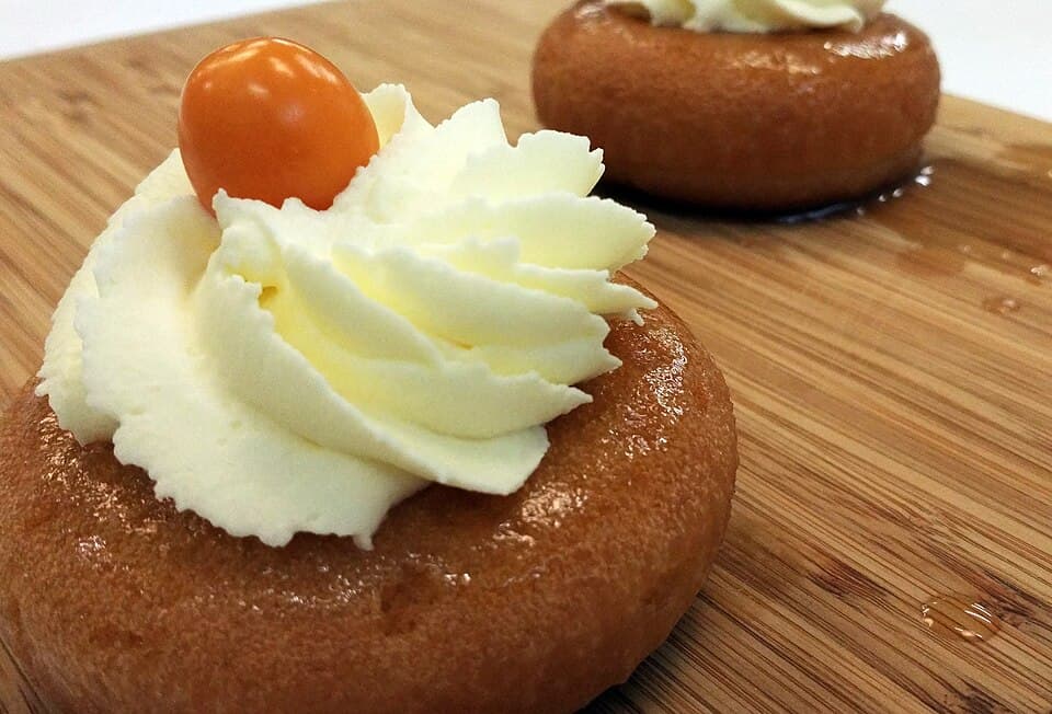 Petits gâteaux imbibés de rhum garnis de crème fouettée sur une planche en bois.