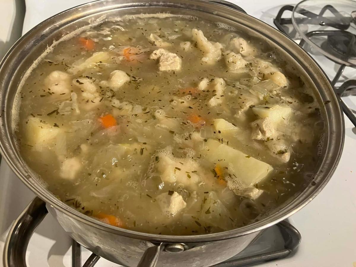 Topf mit klarem Hähncheneintopf, Kartoffelstücken und Klößen.