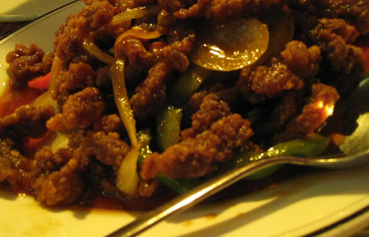 Close-up of crispy sauced beef strips with onions and peppers on a plate.