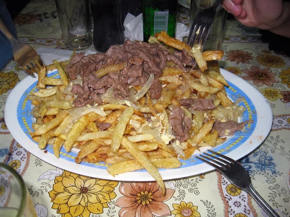 Plato grande de papas fritas cubiertas con tiras de carne y cebollas fritas.