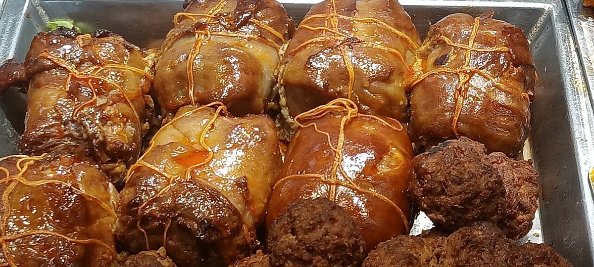 Potongan daging babi panggang mengkilap diikat dengan tali di nampan logam.