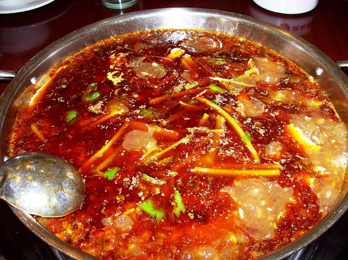 Hot Pot aus Metall, gefüllt mit sprudelnder roter Chilibrühe.
