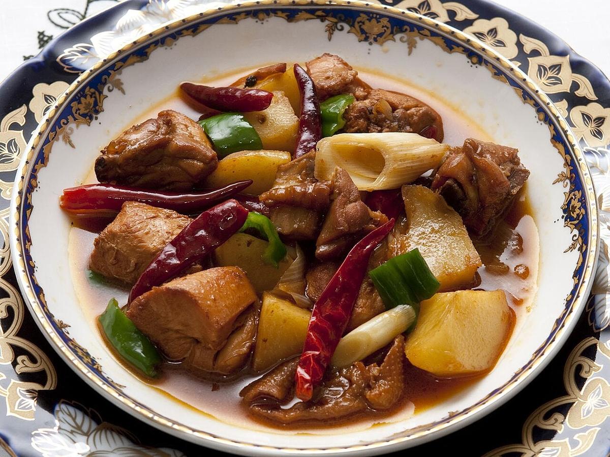 Großer Teller mit Hühner-Eintopf, Kartoffeln, Paprika und getrockneten Chilis.