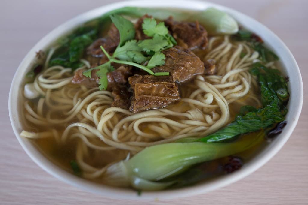 Schüssel mit klarer Rinder-Nudelsuppe mit geschnittenem Rindfleisch, Gemüse und Chiliöl.