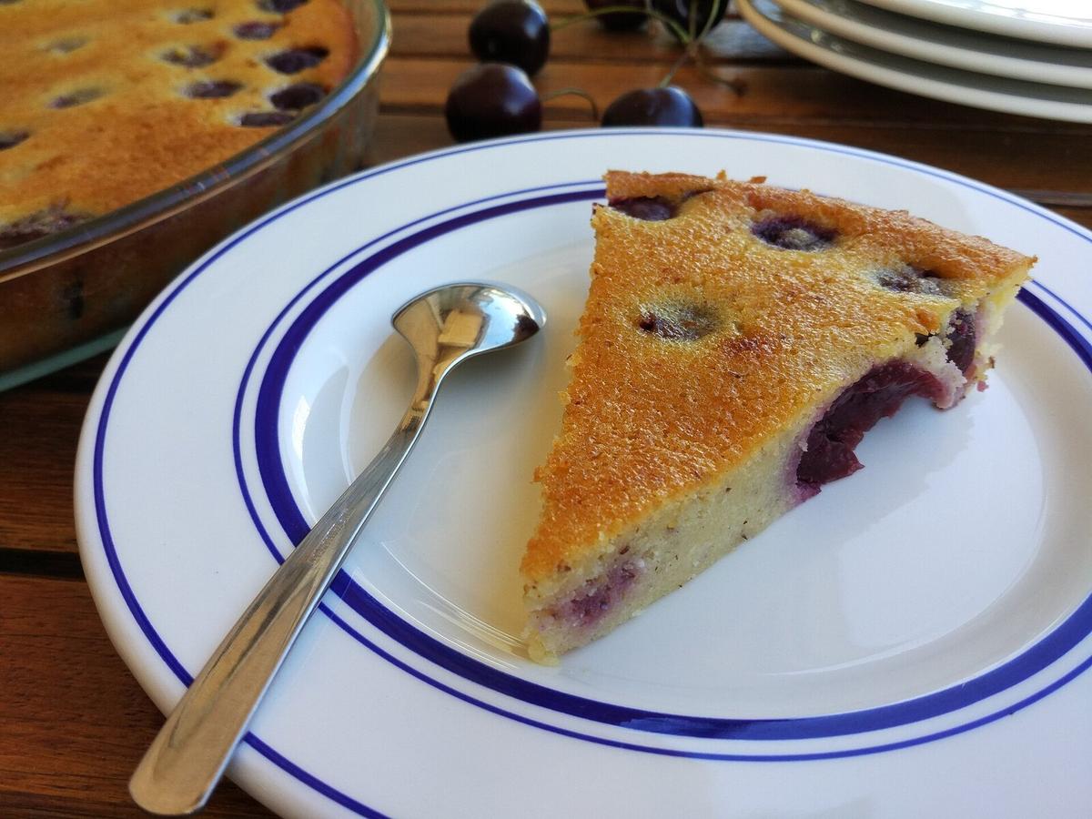 Una rebanada de pastel de natillas de cereza en un plato con cerezas oscuras visibles.