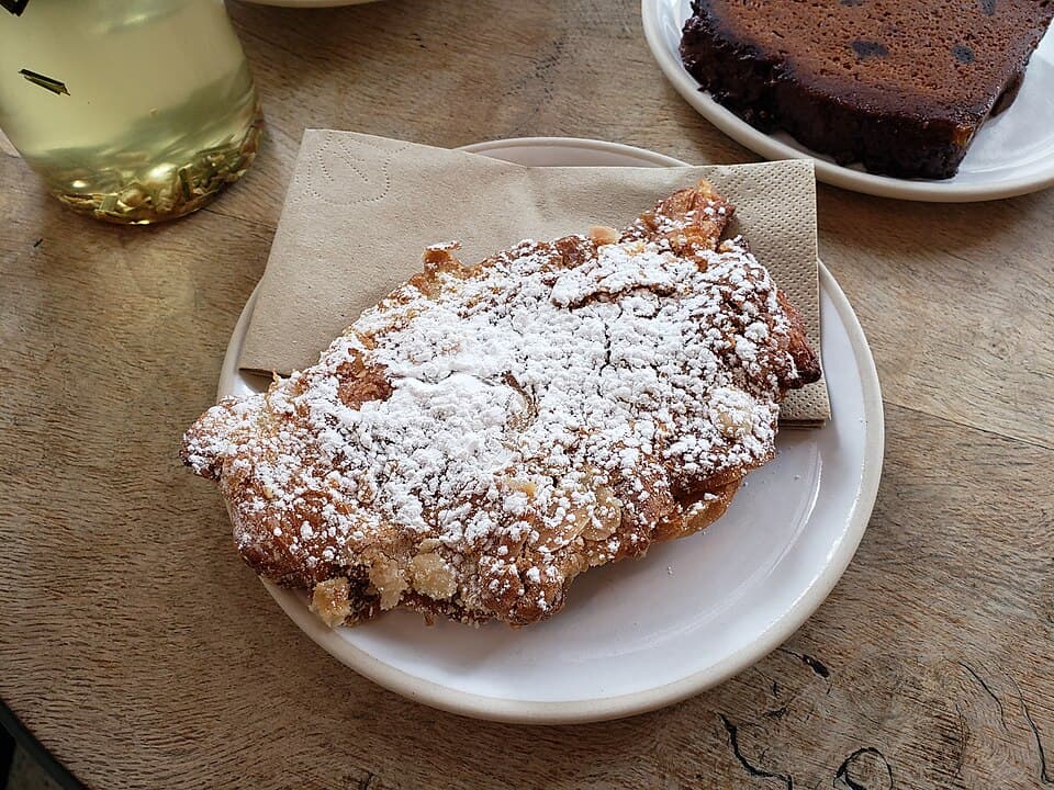 Ein Mandelcroissant, bestäubt mit Puderzucker, auf einem kleinen Teller.