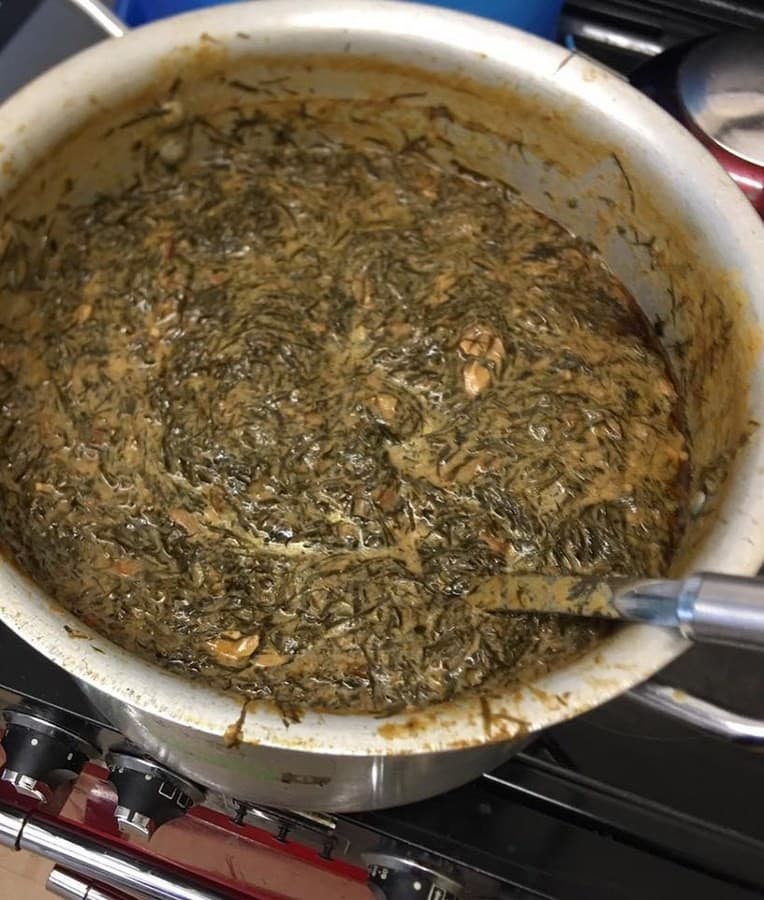Assiette de ragoût de feuilles vertes foncées cuit avec une sauce aux arachides et des morceaux de poisson.