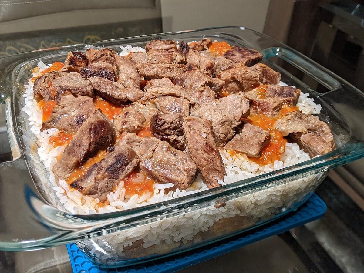 Glasgeschirr mit Schichten aus Reis, Brot, Sauce und Fleischstücken.