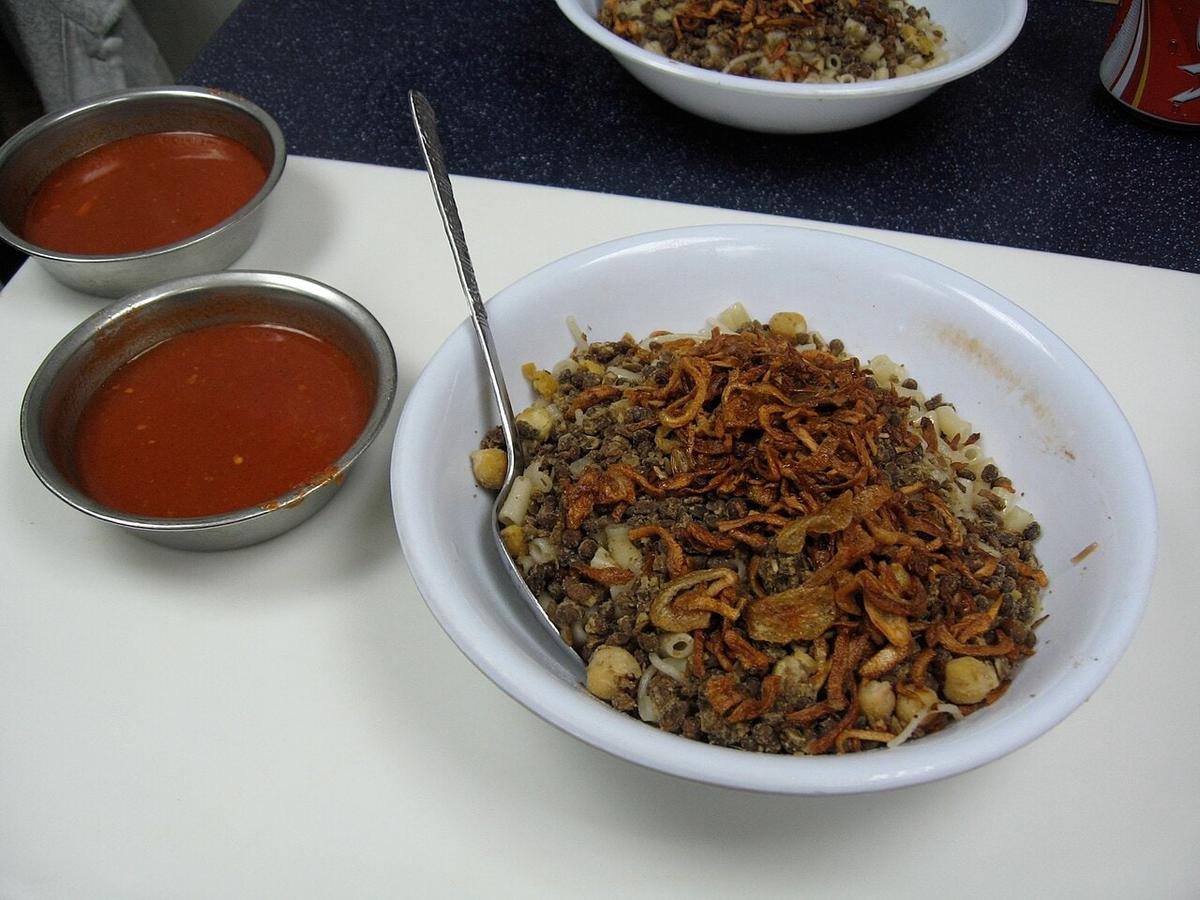Schüssel mit Reis, Linsen, Nudeln, Röstzwiebeln und Kichererbsen mit roten Soßenbechern.