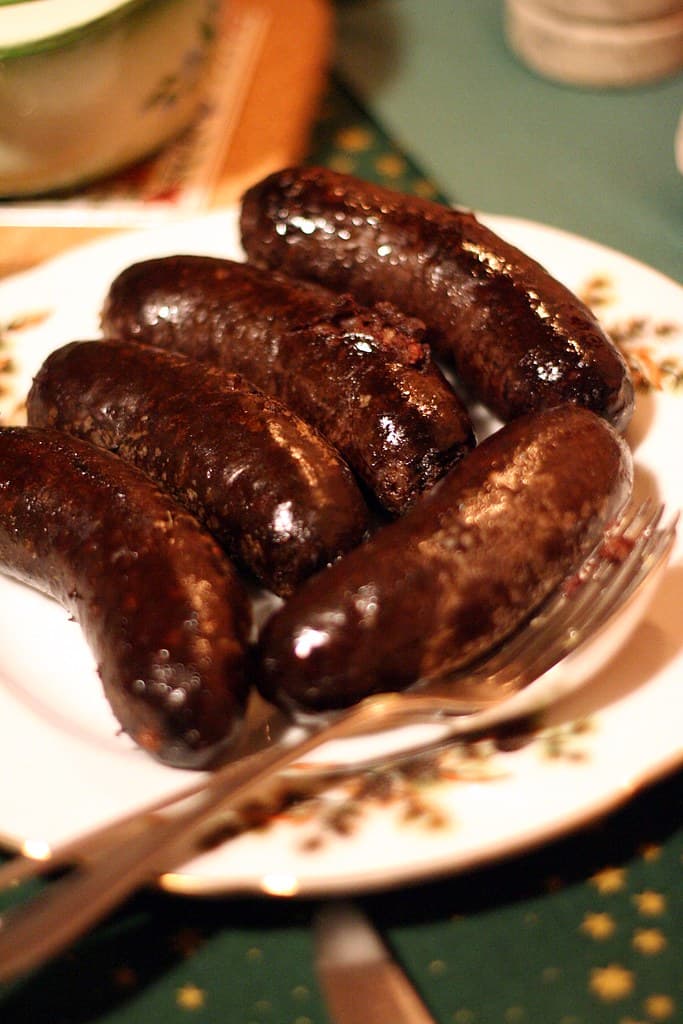 Teller mit dunkel glänzenden Blutwürsten mit einer Gabel.