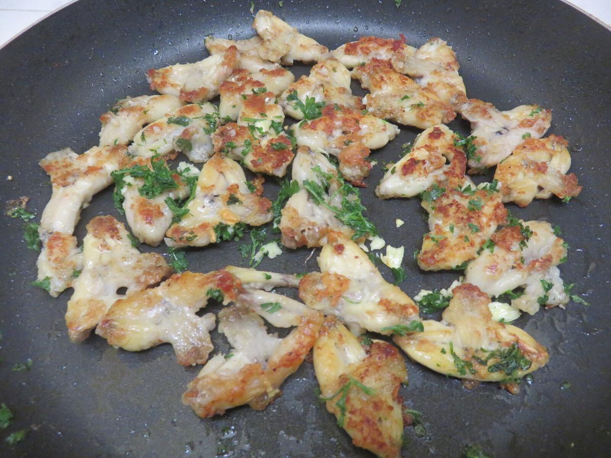 Pan of sautéed frog legs sprinkled with herbs.