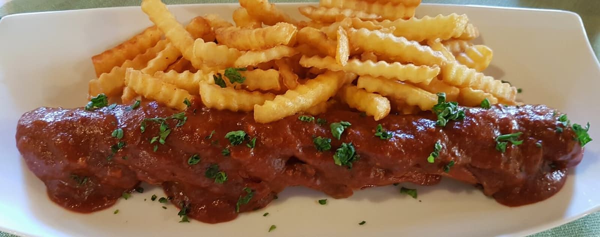 Sausage covered in curry sauce with crinkle-cut fries on a white plate.