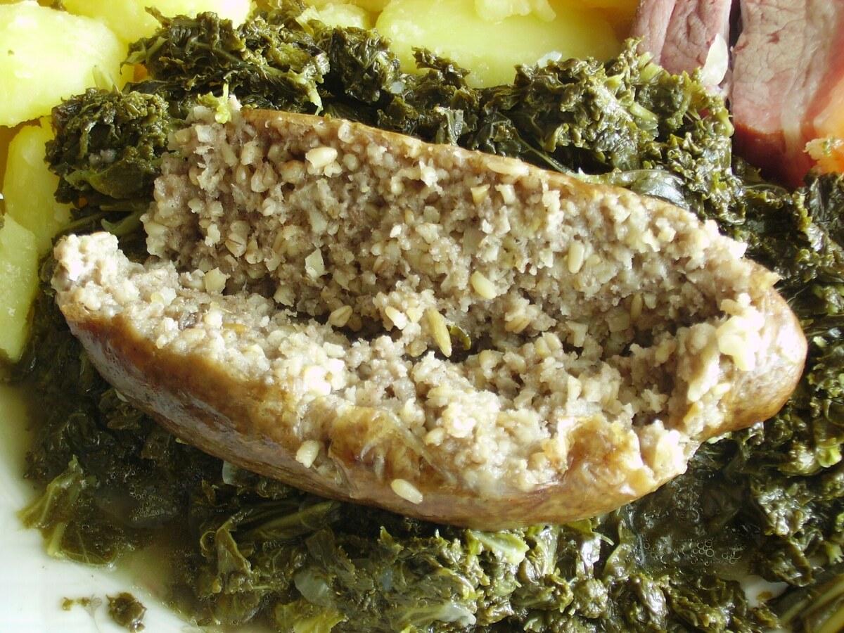 Tranches de saucisse fumée posées sur du chou frisé cuit avec des pommes de terre à côté.