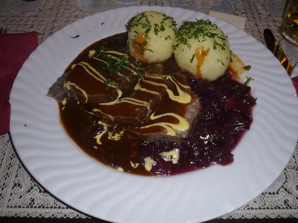 Scheiben geschmortes Rindfleisch in dunkler Soße mit Klößen und Rotkohl.