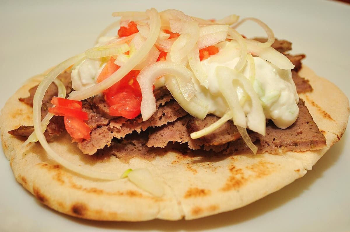 Roti pipih terbuka dengan daging yang diiris, bawang, tomat, dan saus putih.