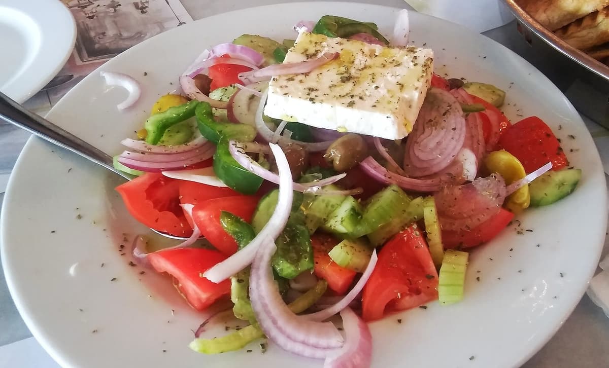 Teller mit stückigen Tomaten, Gurken, Zwiebeln, Oliven und Feta-Käse.