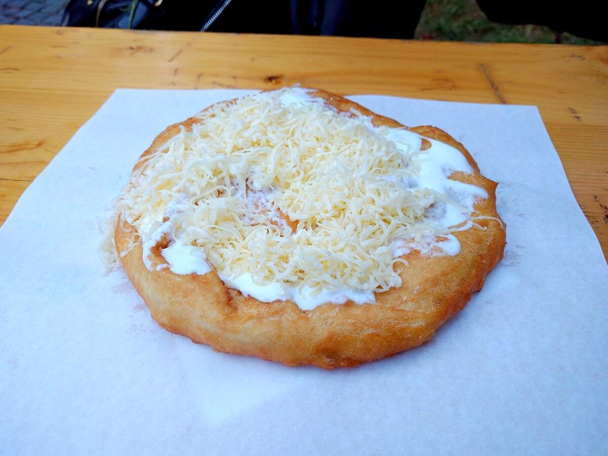Frittiertes Fladenbrot mit Sauerrahm und geriebenem Käse auf weißem Papier.