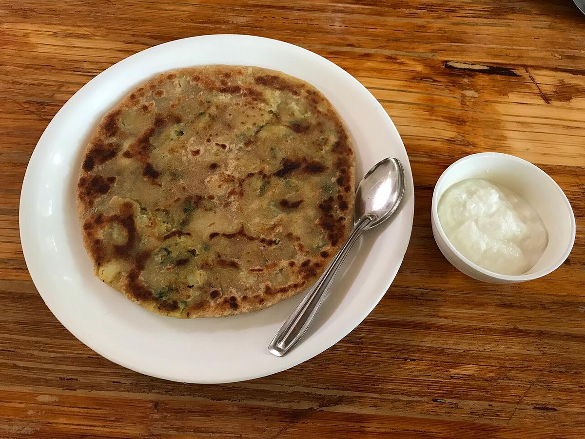 Plate with a browned stuffed flatbread and a small bowl of yogurt.