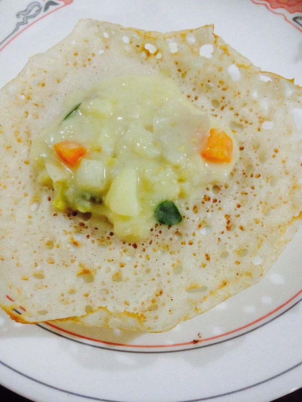 Durchlöcherter Reis-Pfannkuchen mit hellem Kokos-Gemüseeintopf, der sich in der weichen Mitte sammelt.