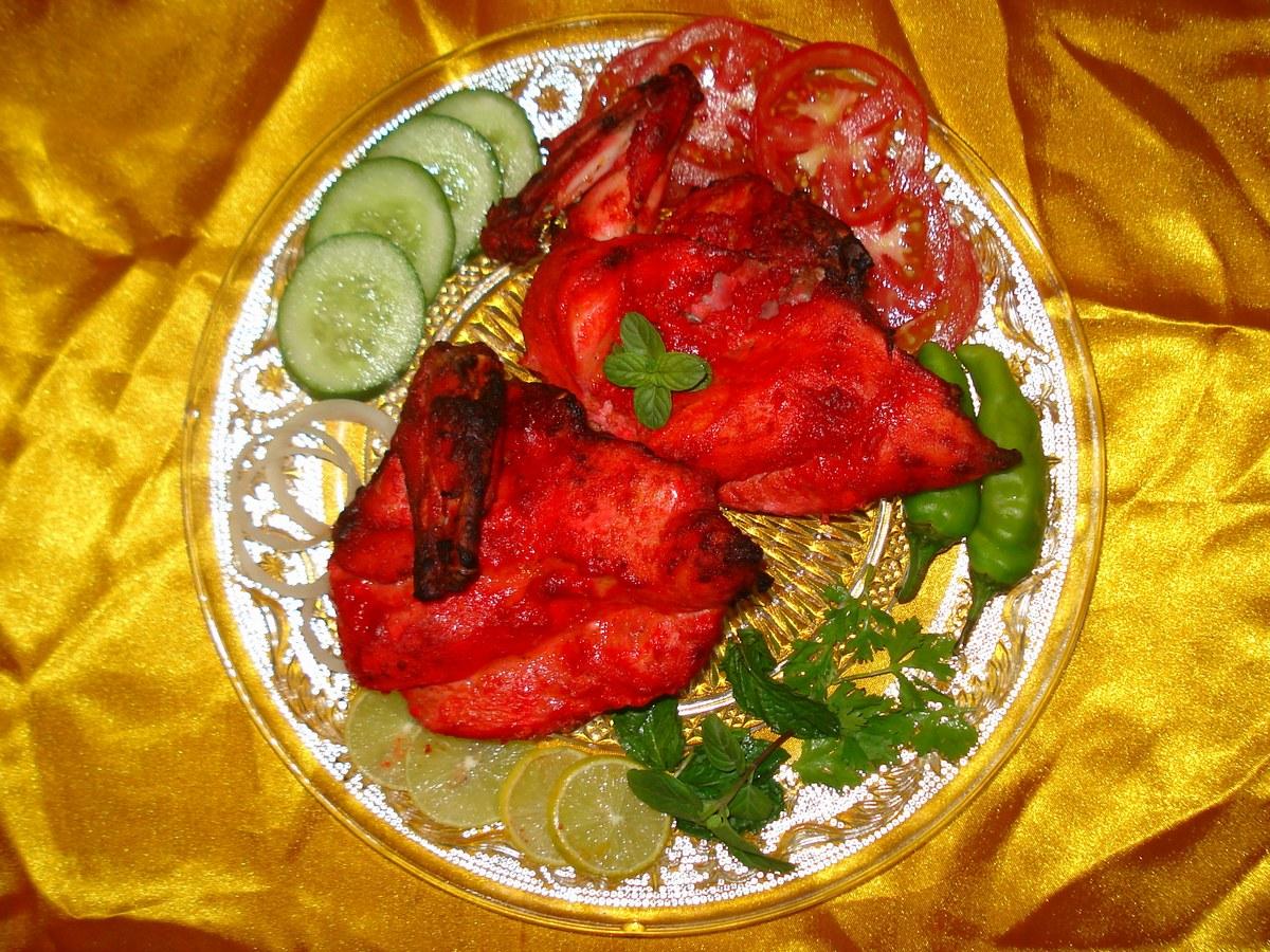 Piezas de pollo asado rojo-anaranjado con guarnición de lima y pepino.