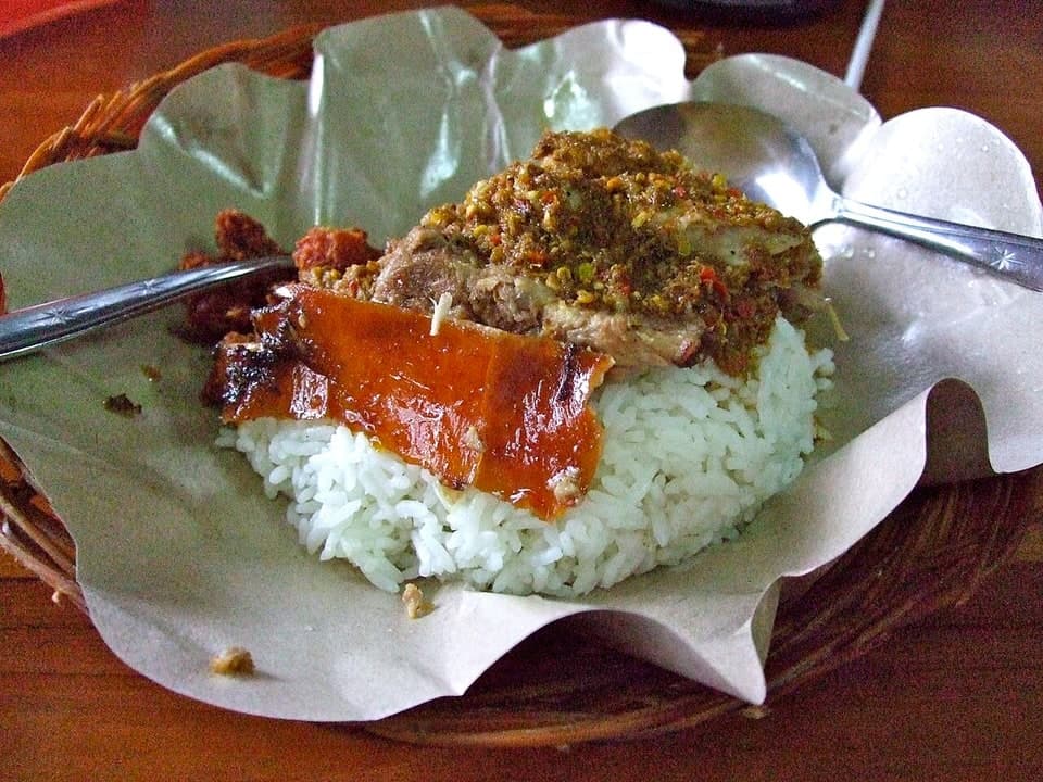 Cerdo asado con arroz, piel crujiente, verduras y salsa en un plato.