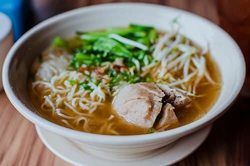 Bowl of clear meatball noodle soup with herbs and bean sprouts.