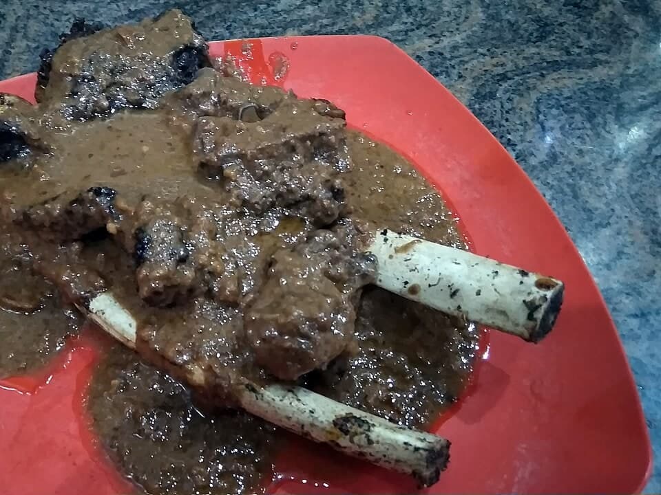 Costillas de res a la parrilla cubiertas con salsa espesa y oscura en un plato sencillo.
