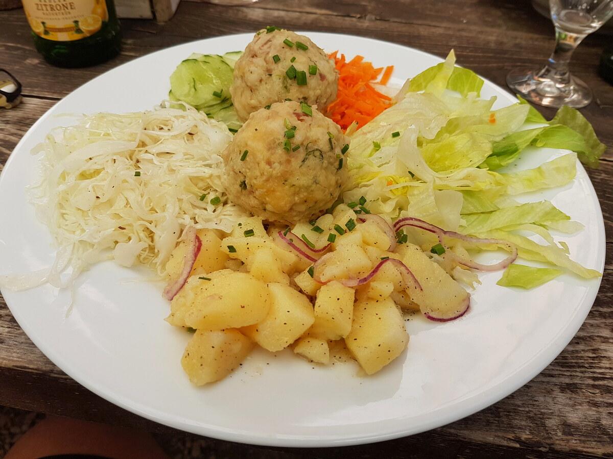 Brotknödel mit Salat und Kartoffeln auf weißem Teller.