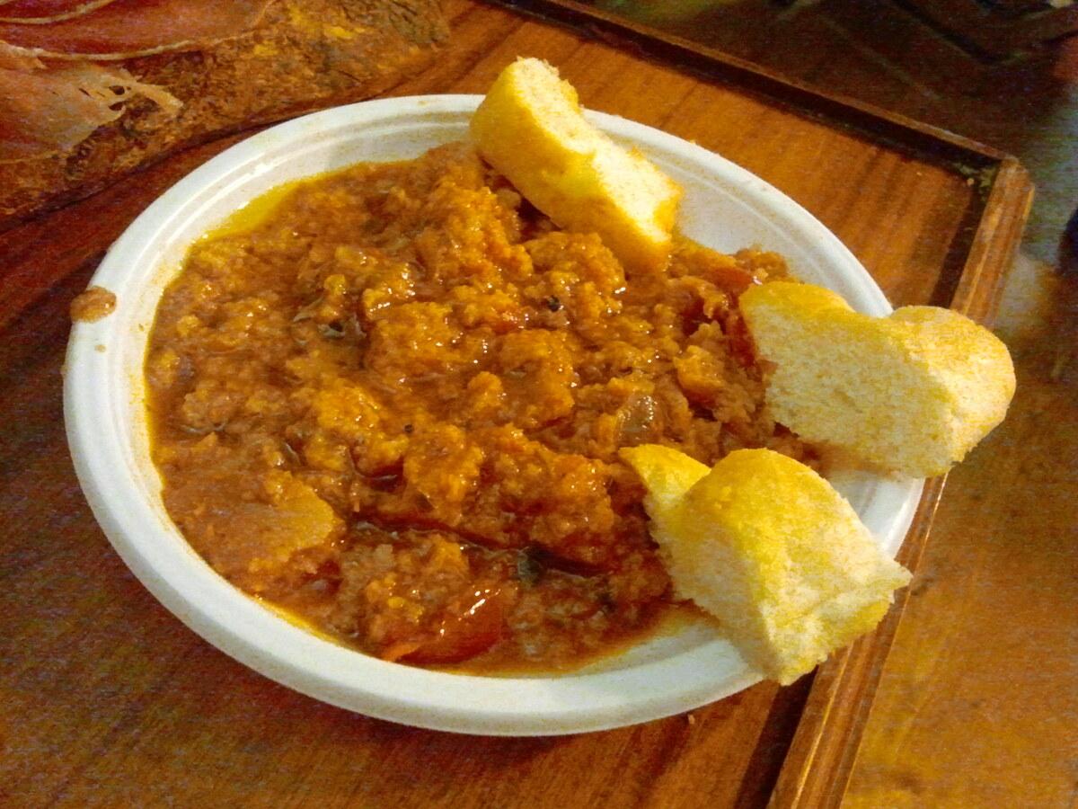 Schüssel mit dicker Tomaten-Brot-Suppe und Brotwürfeln daneben.