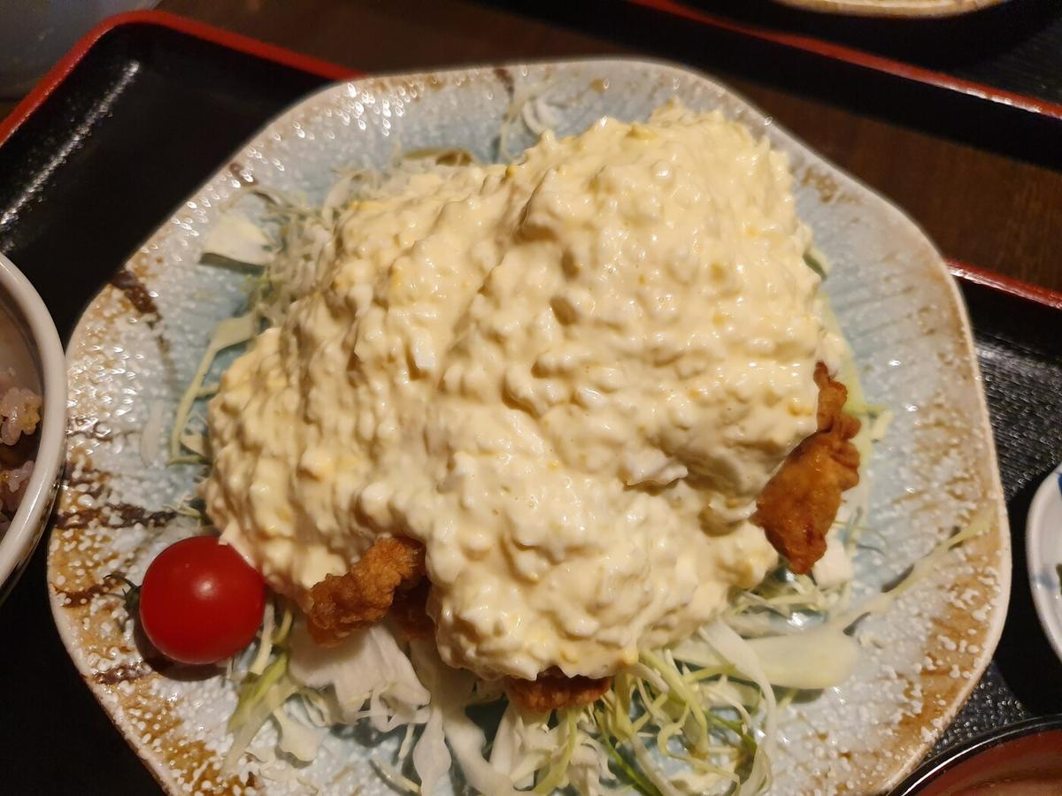 Frittiertes Huhn mit Tartarsoße auf einem Teller, mit geraspeltem Kohl und einer kleinen Tomate.