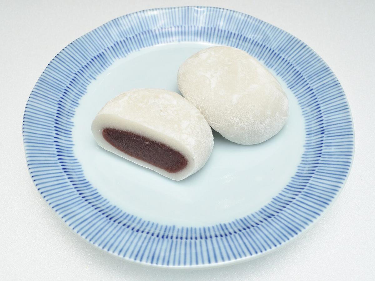 Zwei weiße Mochis auf einem Teller, eines aufgeschnitten, um die rote Bohnenfüllung zu zeigen.