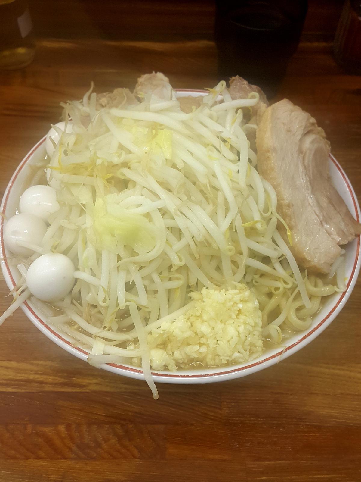 Eine große Ramen-Schüssel, hoch beladen mit Sojasprossen, Knoblauch, Schweinefleisch und dicken Nudeln.