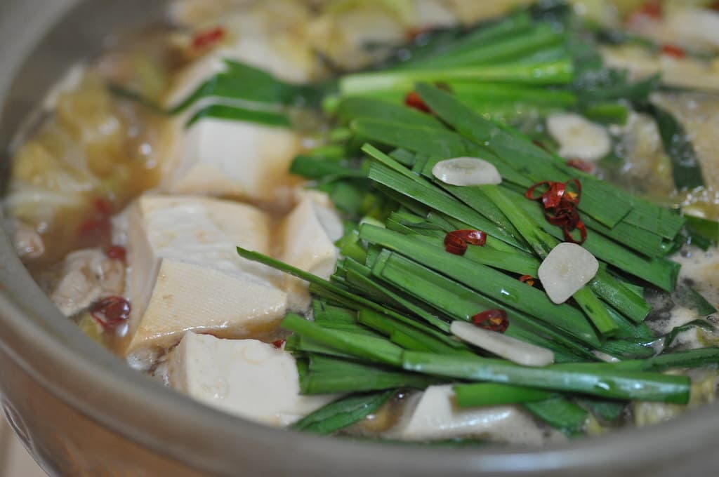 Nahaufnahme eines Hot Pots mit Schnittlauch, Tofu, Kohl, Innereien, Knoblauchscheiben und rotem Chili.