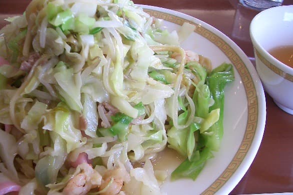 Sepiring mie yang ditutupi kol, daging babi, seafood, dan saus kental mengkilap.