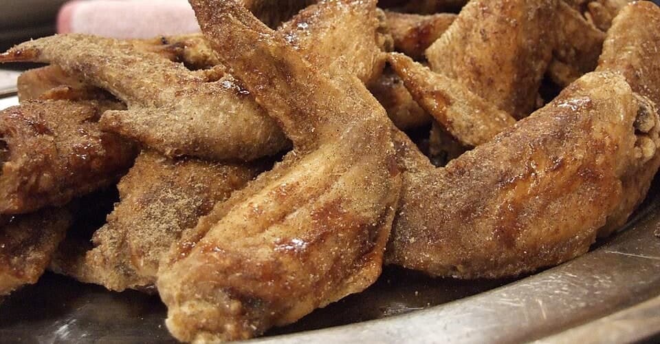 Nahaufnahme von pfeffrigen, frittierten Hähnchenflügeln auf einem Teller.