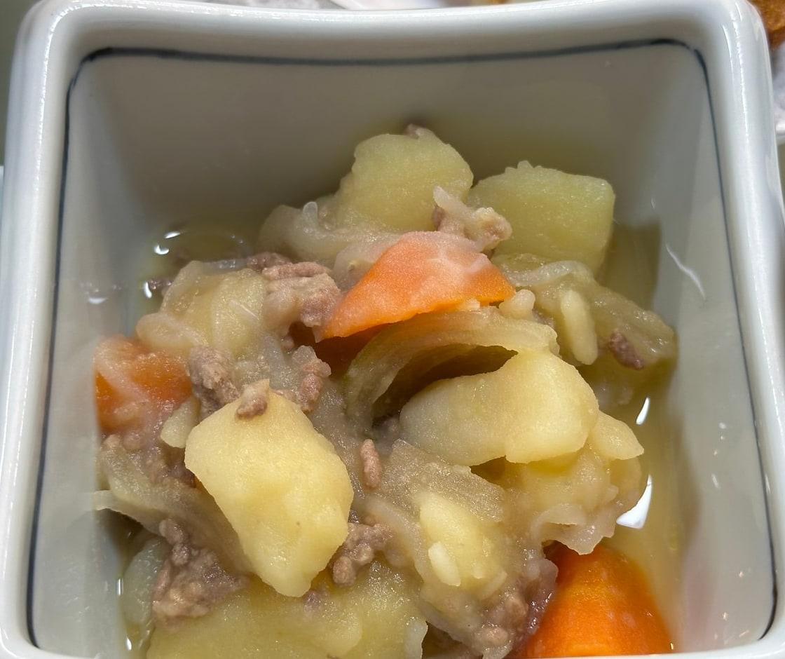 Schale mit Kartoffeln, Fleisch, Zwiebeln und Karotten in heller Brühe.