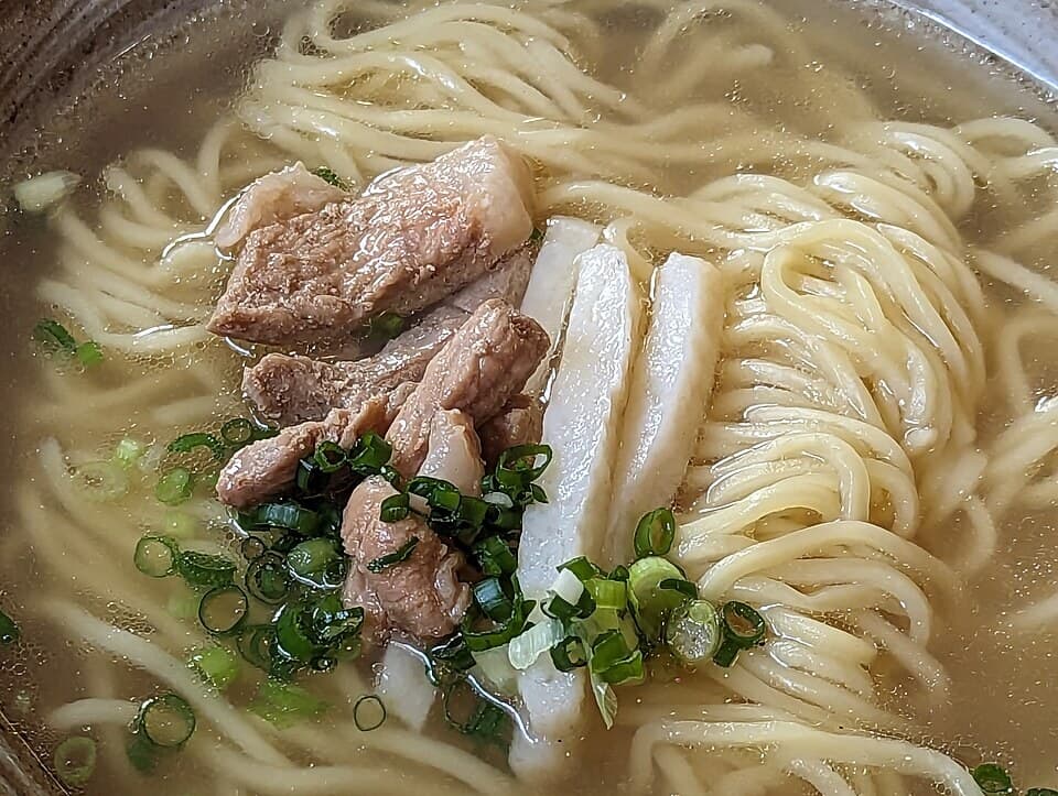 Schüssel mit dicken Weizennudeln in klarer Brühe, Schweinefleischscheiben, Frühlingszwiebeln und Fischkuchen.