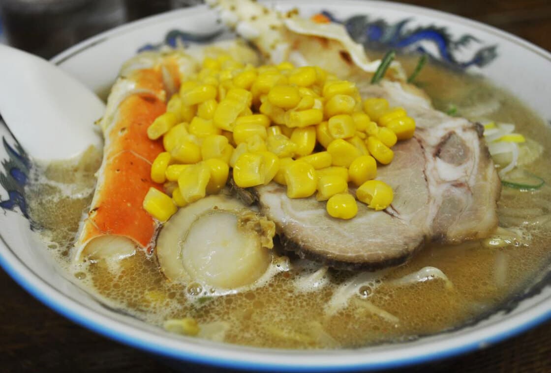 Schüssel mit Miso-Ramen, garniert mit Mais, Schweinefleischscheiben, Krabben, Jakobsmuscheln, Nudeln und Brühe.