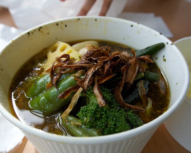 Mangkok sup kari dengan sayuran di samping porsi kecil nasi.