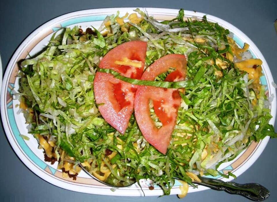 طبق من الأرز مغطى بلحم مفروم متبل، خس مفروم، شرائح طماطم، وجبن.