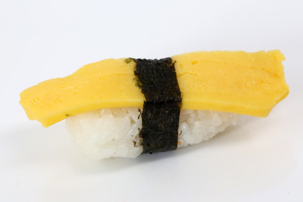 Ein einzelnes Stück Eieromelett-Sushi, gebunden mit Algen auf weißem Hintergrund.