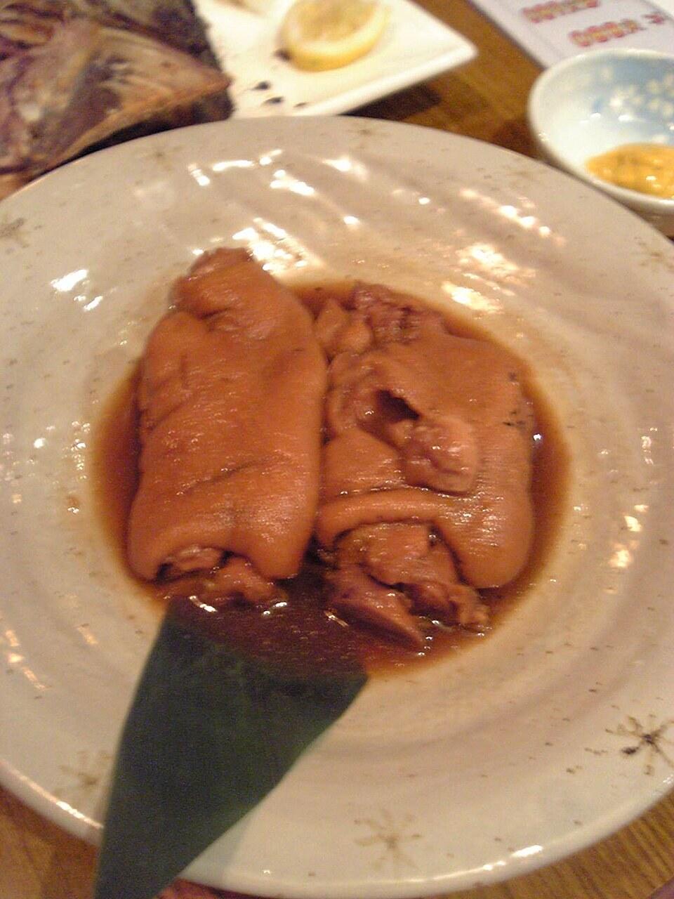 Kleiner Teller mit glänzend geschmortem Schweinefuß in brauner Sauce, mit Löffel.