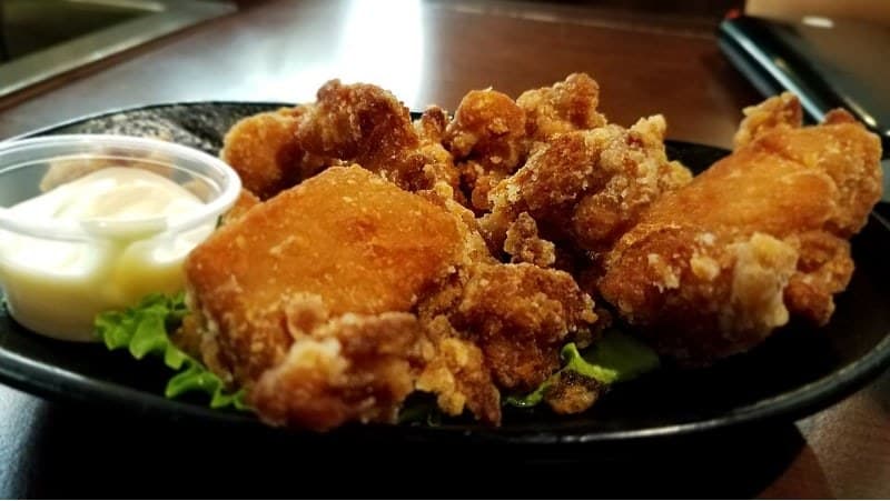Knusprige frittierte Hähnchenstücke, serviert auf einem schwarzen Teller mit einer kleinen Schale Sauce.