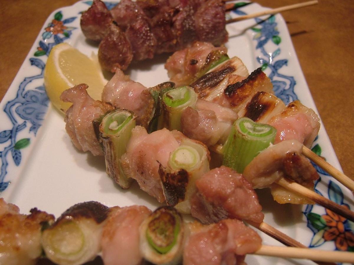 Gegrillte Hähnchen- und Frühlingszwiebelspieße auf einem rechteckigen Teller mit Zitrone.
