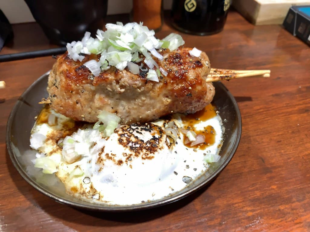 Gegrillter Hühnerfleischbällchenspieß mit gehackten Frühlingszwiebeln und Soße.