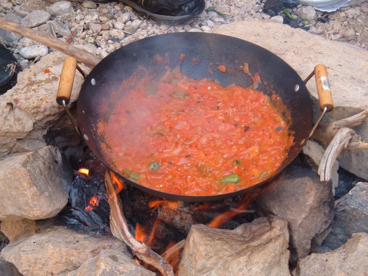 Rote Tomatenmischung köchelt in einer schwarzen Pfanne über offenem Feuer.