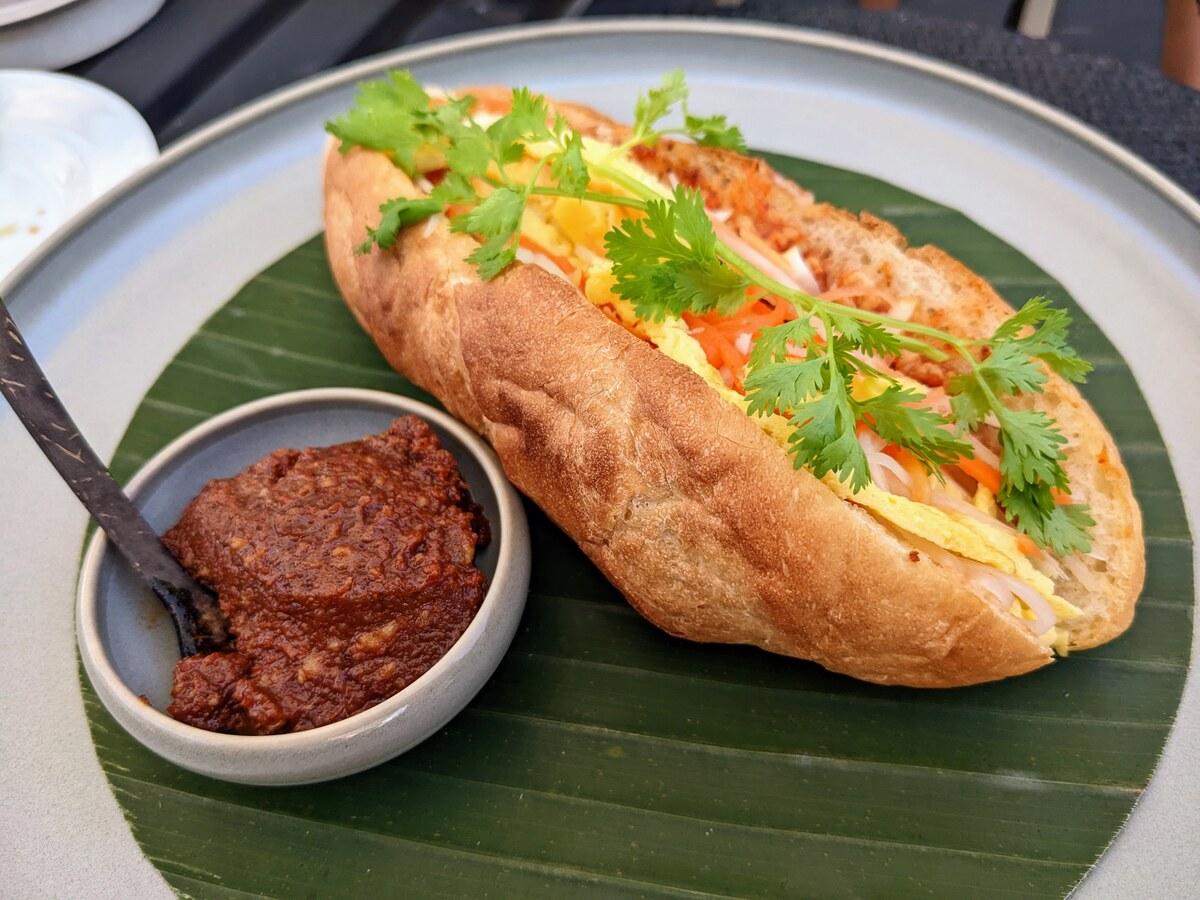 Gefülltes Baguette-Sandwich mit Kräutern und Chilipaste auf einem schlichten Teller.