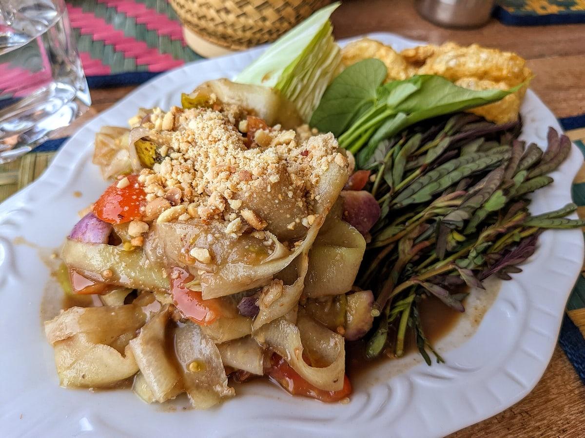 Teller mit geraspeltem grünen Papayasalat mit Tomaten, langen Bohnen, Auberginen, Chili und zerstoßenen Erdnüssen.